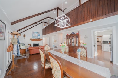 Dining area with high vaulted ceiling, dark wood-style floors, beamed ceiling, a fireplace, and a chandelier