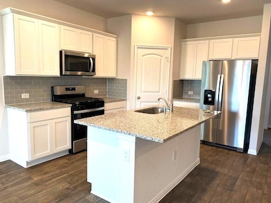 Kitchen featuring stainless steel appliances, white cabinets, light stone counters, and dark wood-type flooring