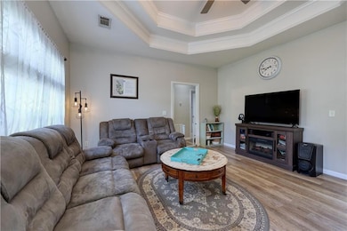 Living area featuring light wood finished floors, a raised ceiling, ceiling fan, crown molding, and baseboards