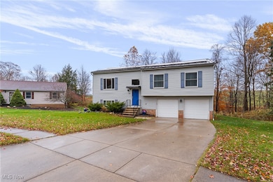 Raised ranch with a front lawn, brick siding, concrete driveway, and an attached garage