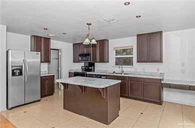 Kitchen with black appliances, a kitchen bar, hanging light fixtures, and light tile patterned floors