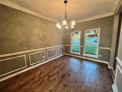 Unfurnished dining area featuring dark wood-style flooring, ornamental molding, a decorative wall, and a chandelier