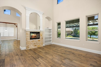 Unfurnished library/sitting area with a stone fireplace, a high ceiling, healthy amount of natural light, and dark wood-style floors