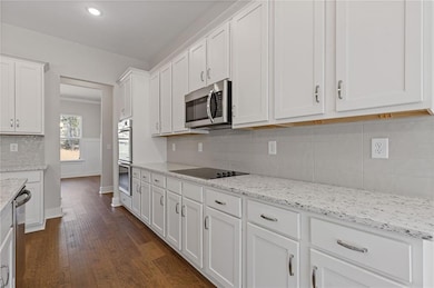 Kitchen featuring white cabinets, dark wood finished floors, backsplash, light stone counters, and stainless steel appliances