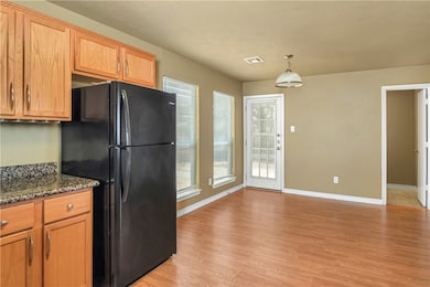 Kitchen featuring freestanding refrigerator, light wood finished floors, brown cabinetry, dark stone countertops, and decorative light fixtures