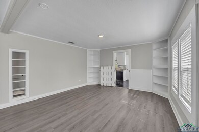 Unfurnished living room with built in features, a textured ceiling, wood finished floors, baseboards, and crown molding