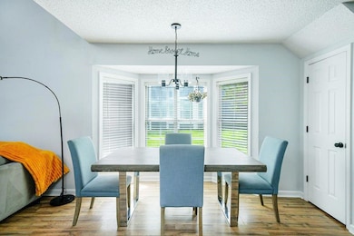 Dining space featuring a chandelier, a textured ceiling, wood finished floors, and lofted ceiling