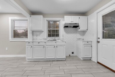 Kitchen with white cabinets, backsplash, under cabinet range hood, and light stone countertops