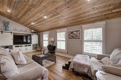 Living area with vaulted ceiling, a barn door, wood ceiling, recessed lighting, and light wood-style floors