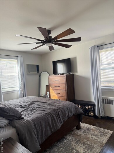 Bedroom with multiple windows, wood finished floors, radiator, and ceiling fan