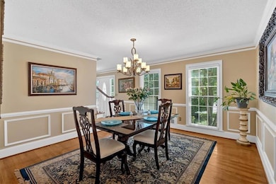 Dining area with a chandelier, a textured ceiling, crown molding, wainscoting, and light wood-style flooring