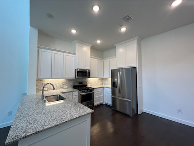 Kitchen featuring white cabinets, stainless steel appliances, light stone countertops, decorative backsplash, and a peninsula