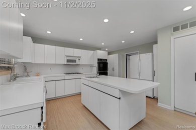 Kitchen featuring light countertops, white appliances, white cabinetry, recessed lighting, and light wood finished floors