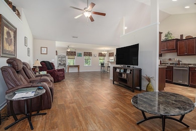 Living area featuring ceiling fan, light wood-style flooring, a chandelier, high vaulted ceiling, and baseboards