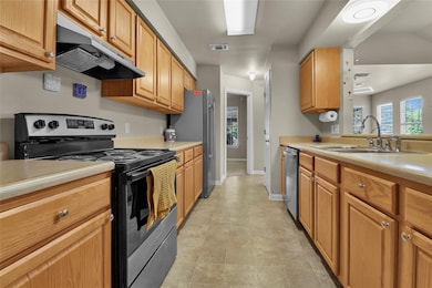 Kitchen featuring appliances with stainless steel finishes, under cabinet range hood, light countertops, and brown cabinets