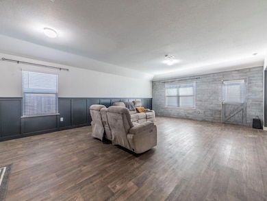 Living area featuring plenty of natural light, dark wood-type flooring, a textured ceiling, wainscoting, and a decorative wall