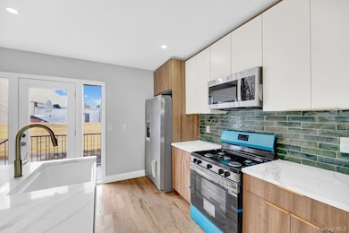 Kitchen with modern cabinets, appliances with stainless steel finishes, light stone countertops, light wood-style flooring, and recessed lighting