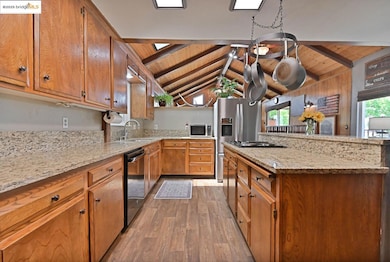 Kitchen featuring wood ceiling, light stone countertops, brown cabinetry, light wood-style floors, and stainless steel appliances