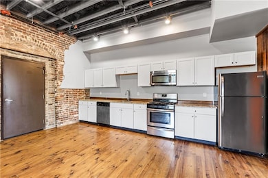 Kitchen featuring appliances with stainless steel finishes, brick wall, a sink, white cabinets, and light wood-type flooring