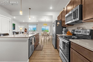 Kitchen featuring appliances with stainless steel finishes, light wood-type flooring, recessed lighting, light countertops, and decorative light fixtures