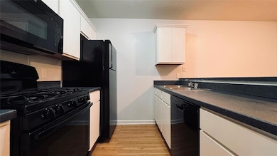 Kitchen with black appliances, white cabinetry, d