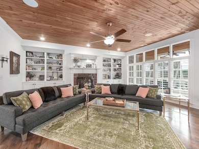 Living area with wooden ceiling, built in shelves, a ceiling fan, a brick fireplace, and wood finished floors