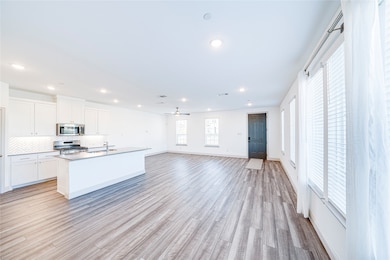 Kitchen with white cabinets, open floor plan, appliances with stainless steel finishes, an island with sink, and tasteful backsplash