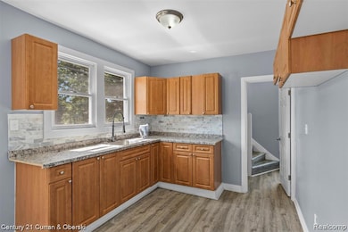 Kitchen with light stone countertops, light wood finished floors, tasteful backsplash, and brown cabinets
