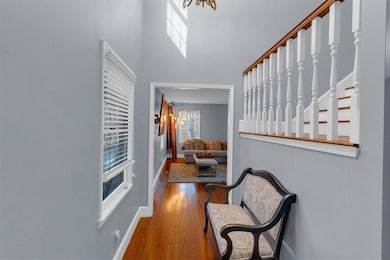 Hall with a towering ceiling, stairway, wood finished floors, a chandelier, and baseboards