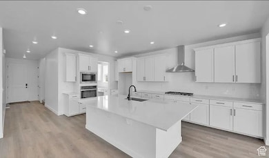 Kitchen with white cabinetry, recessed lighting, light wood-style flooring, a kitchen island with sink, and wall chimney exhaust hood