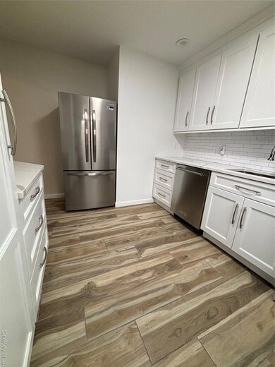 Kitchen with white cabinetry, white refrigerator, light wood-type flooring, and tasteful backsplash