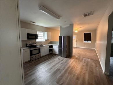 Kitchen with appliances with stainless steel finishes, a sink, light wood-style flooring, white cabinets, and light countertops