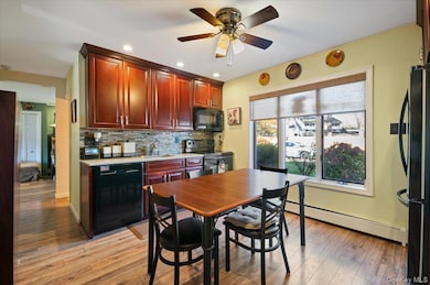 Kitchen with cherry brown cabinets, backsplash, black appliances, recessed lighting, and laminate flooring.