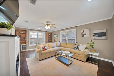 Living area with crown molding, healthy amount of natural light, dark wood-style flooring, and ceiling fan