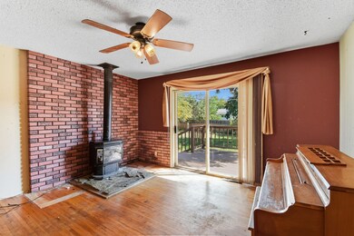 Unfurnished living room with a wood stove, hardwood / wood-style floors, a textured ceiling, ceiling fan, and brick wall