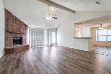 Unfurnished living room featuring ceiling fan, a textured ceiling, beamed ceiling, a fireplace, and wood finished floors