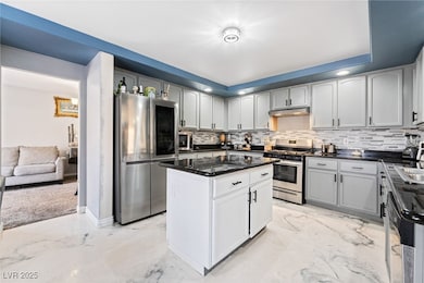 Kitchen featuring appliances with stainless steel finishes, a center island, backsplash, under cabinet range hood, and dark stone counters