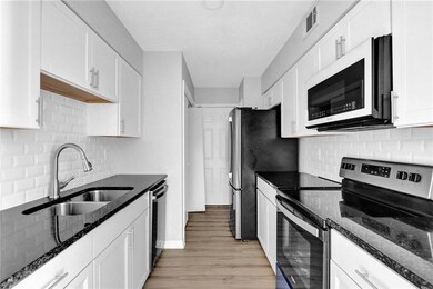 Kitchen featuring stainless steel appliances, white cabinets, light wood-style floors, dark stone counters, and tasteful backsplash