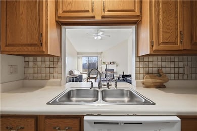 Kitchen view of decorative backsplash, light countertops, brown cabinets, dishwasher, and a ceiling fan