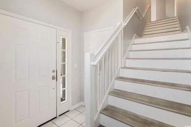 Foyer entrance featuring stairs, light tile patterned floors, and baseboards