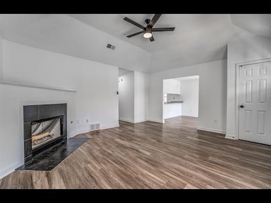 Unfurnished living room with ceiling fan, lofted ceiling, a tiled fireplace, wood finished floors, and baseboards