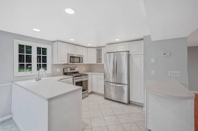 Kitchen featuring a peninsula, stainless steel appliances, light countertops, white cabinetry, and recessed lighting