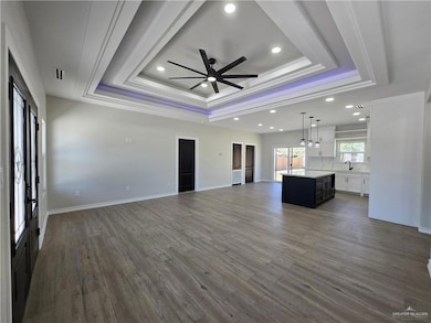 Unfurnished living room with a raised ceiling, a ceiling fan, recessed lighting, dark wood-type flooring, and crown molding