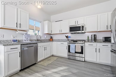 Kitchen featuring appliances with stainless steel finishes, white cabinetry, and light stone countertops