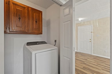 Laundry room with a textured ceiling, washer / dryer, light wood-style floors, and cabinet space