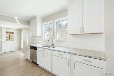 Kitchen with white cabinets, light wood-style flooring, ornamental molding, a sink, and stainless steel dishwasher