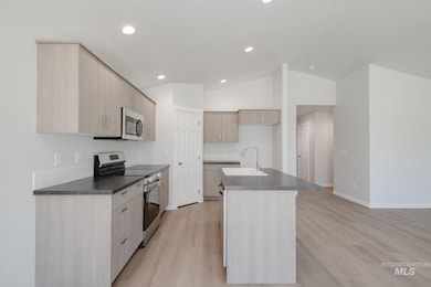 Kitchen featuring dark countertops, appliances with stainless steel finishes, light brown cabinetry, a center island with sink, and light wood finished floors