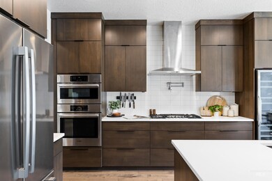 Kitchen with appliances with stainless steel finishes, wall chimney range hood, modern cabinets, decorative backsplash, and a textured ceiling