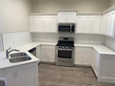 Kitchen featuring stainless steel appliances, white cabinets, light stone countertops, light wood-style floors, and a peninsula