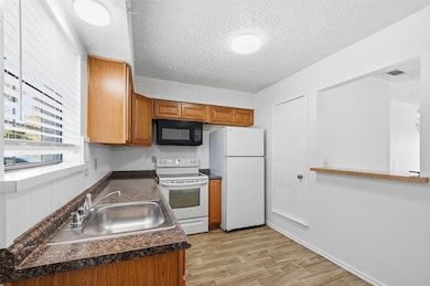 Kitchen with white appliances, dark countertops, wood tiled floors, brown cabinets, and a textured ceiling